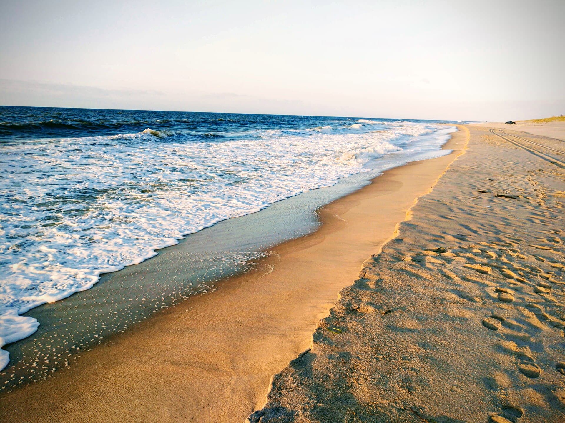 The surf line at Georgica in early-morning light, empty, with vehicle tracks in the dry sand above it. Shot at 6.53am in September, and the file is marked as having camera effects applied, so the sand reads warmer and more golden than it does to the eye.