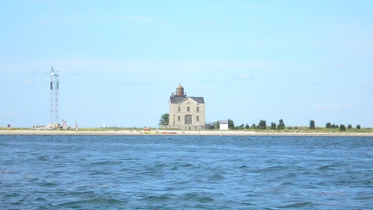 Cedar Point Lighthouse, Hamptons, New York — the granite keeper's house and lantern standing on the far end of the Cedar Point spit, seen across the water.